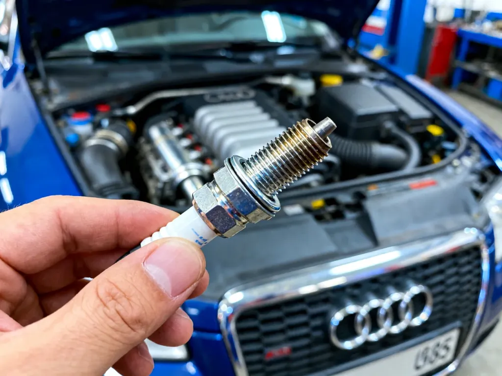 Mechanik trzyma nowy czujnik ciśnienia klimatyzacji na tle otwartej komory silnika Audi A6 C5.