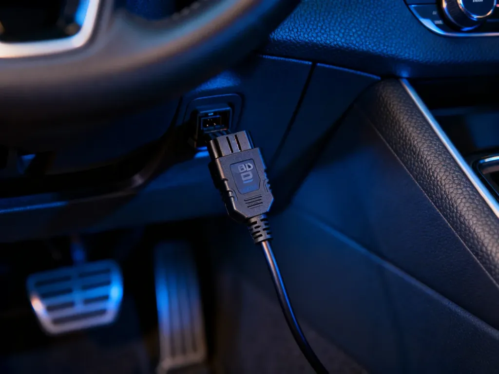 Skaner diagnostyczny OBD2 podłączony do portu pod kierownicą samochodu. Profesjonalne ujęcie w nowoczesnym wnętrzu pojazdu.